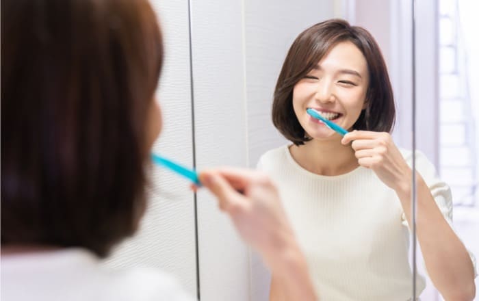 鏡を見ながら歯磨きする女性の画像